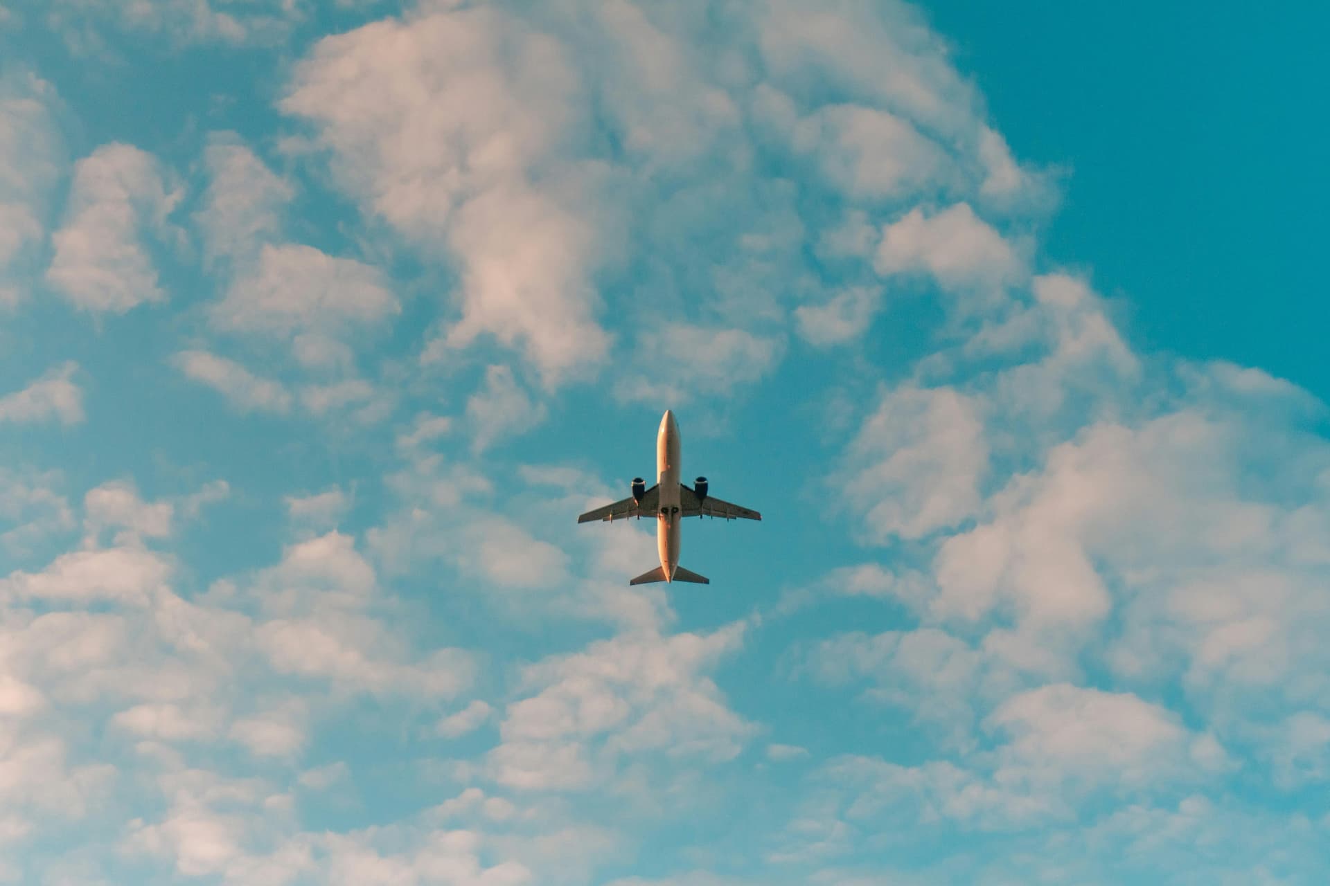 An airplane flies upward, viewed from below, in a slightly cloudy sky with light blue hues.