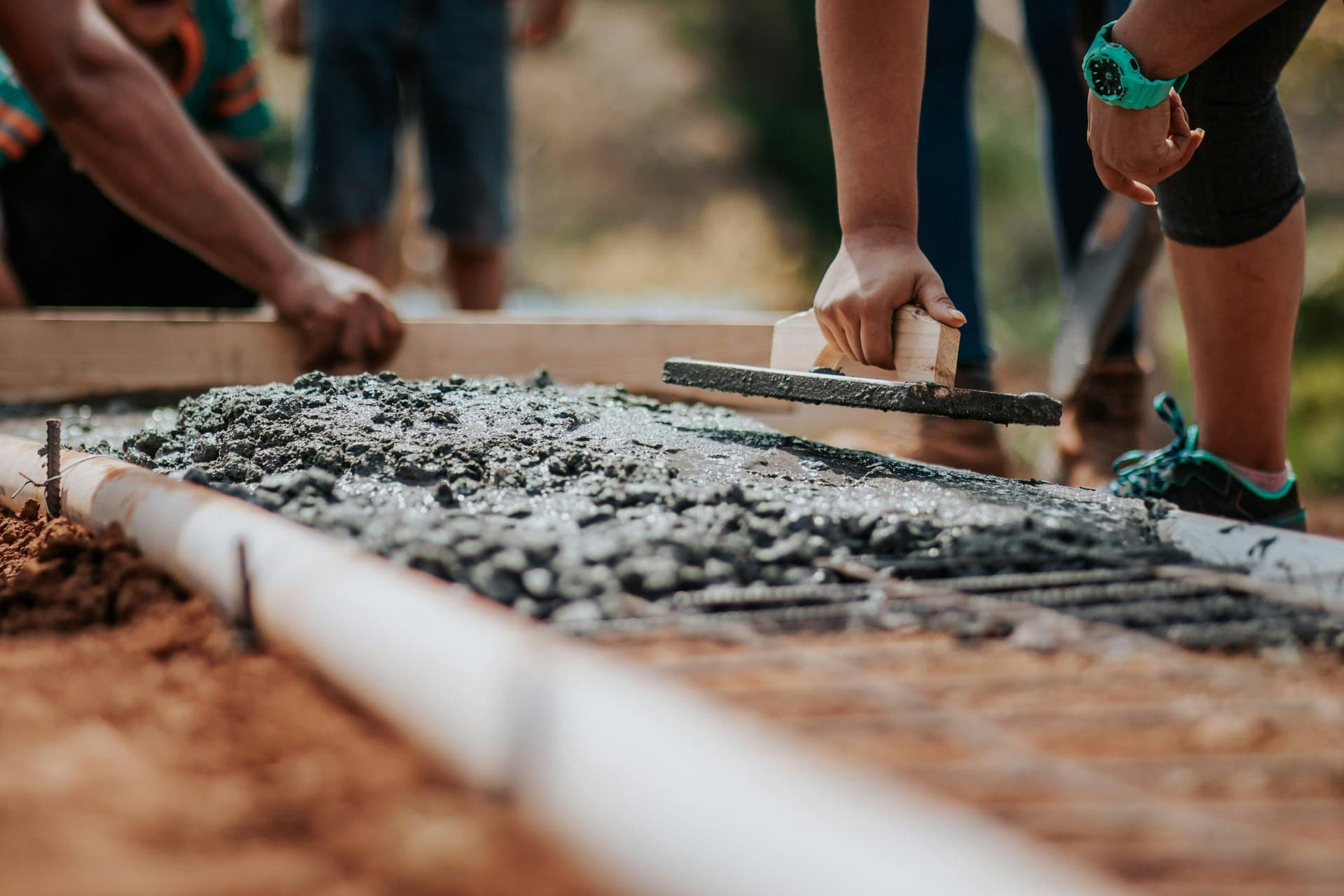 Close-up of workers smoothing wet concrete with tools during a construction project, with focus on the hands and tools in the foreground.