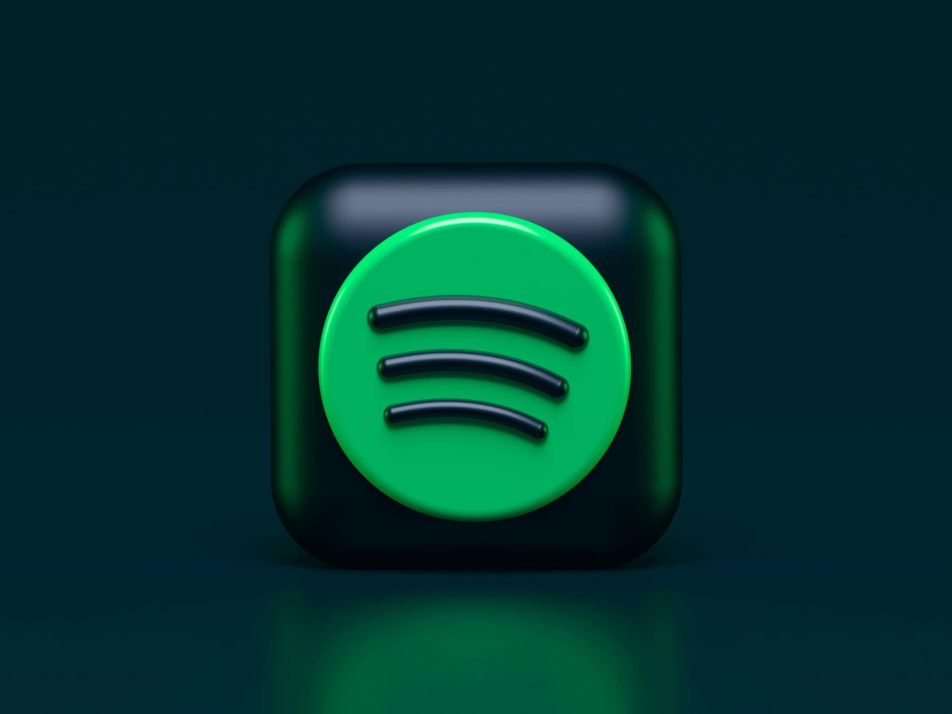 This image features a three-dimensional Spotify logo. The logo is a green circle containing three curved black lines, representing sound waves. The green circle is placed on a dark, rounded square background with a glossy finish. The overall setting is minimal, with a dark green-blue color scheme.