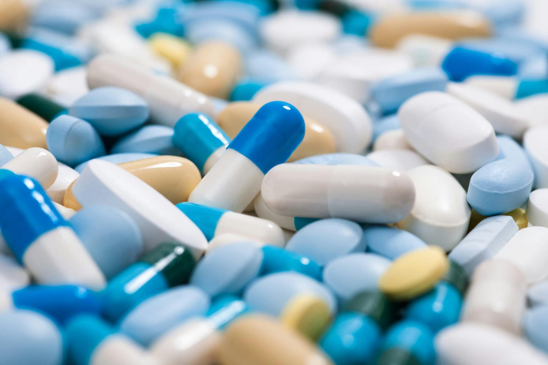 Multicolored pills and capsules lying scattered on a surface, creating a vibrant and cluttered arrangement of various shapes and sizes.