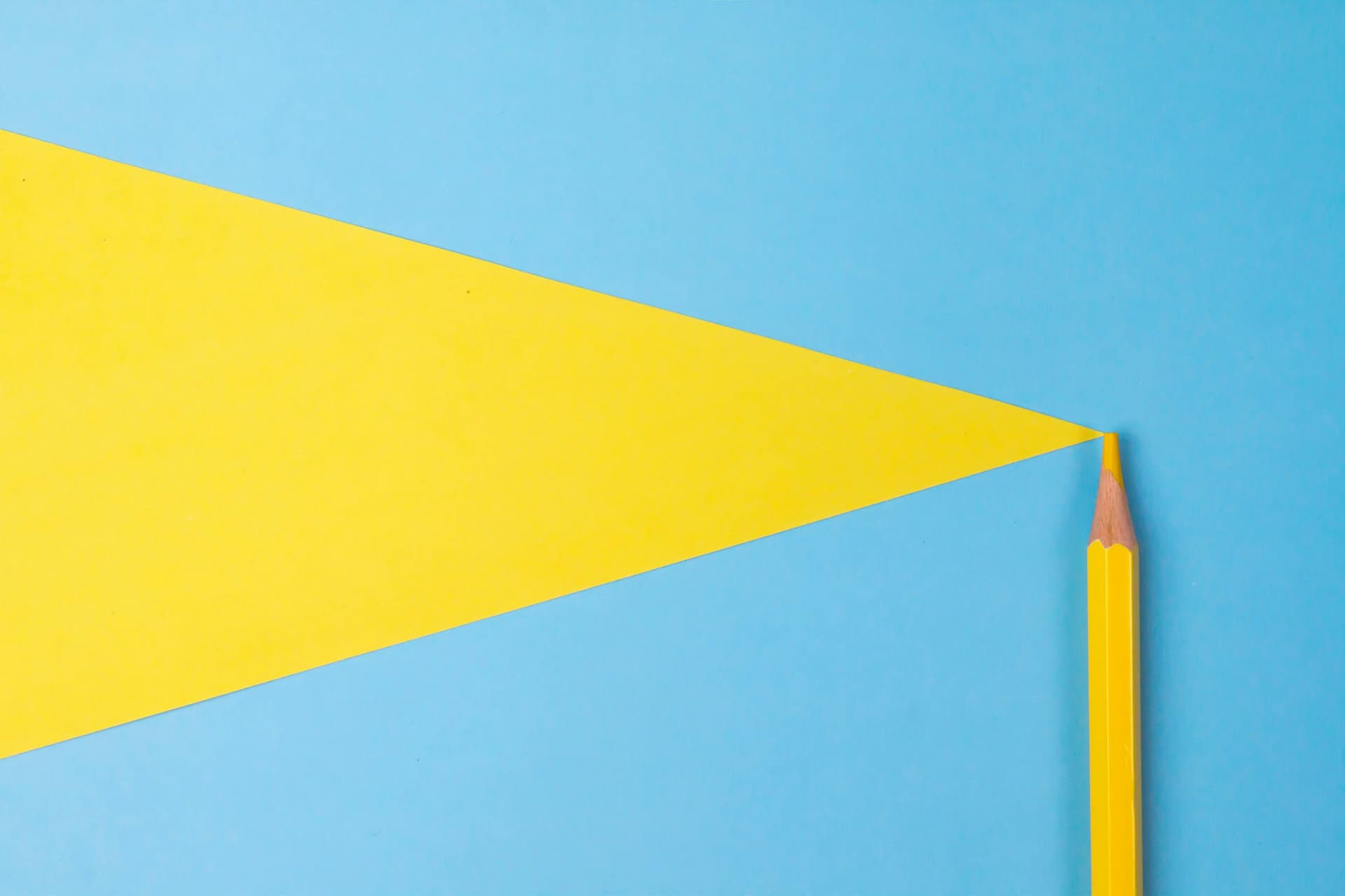 Yellow pencil aligned with a yellow triangle on a blue background, creating the illusion that the pencil extends into the triangle.