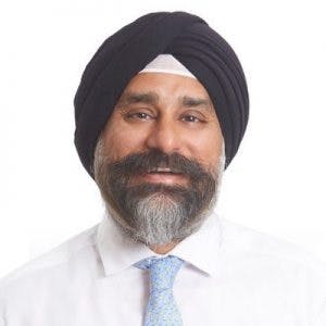 A man with a turban and beard is smiling, wearing a white shirt and blue patterned tie against a plain white background.