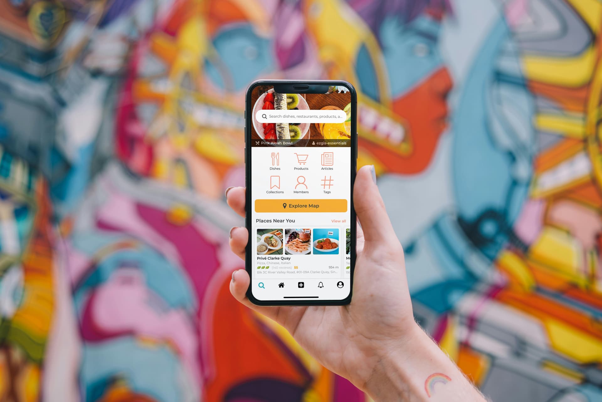 A hand holds a smartphone displaying a delivery app with options for food, groceries, and retail. The background features a vibrant, abstract mural. Text on the screen includes "Restaurants, groceries, pharmacies, more" and "Please Near You."